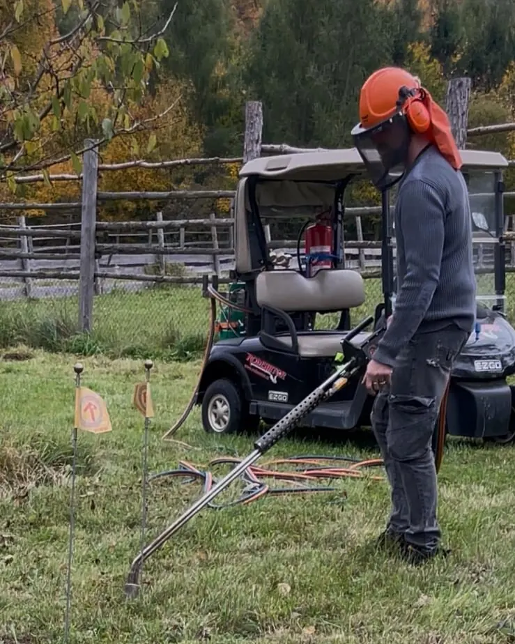 Pracovník v ochranné helmě se štítem ošetřuje Rodenatorem trávník, za ním golfový vozík